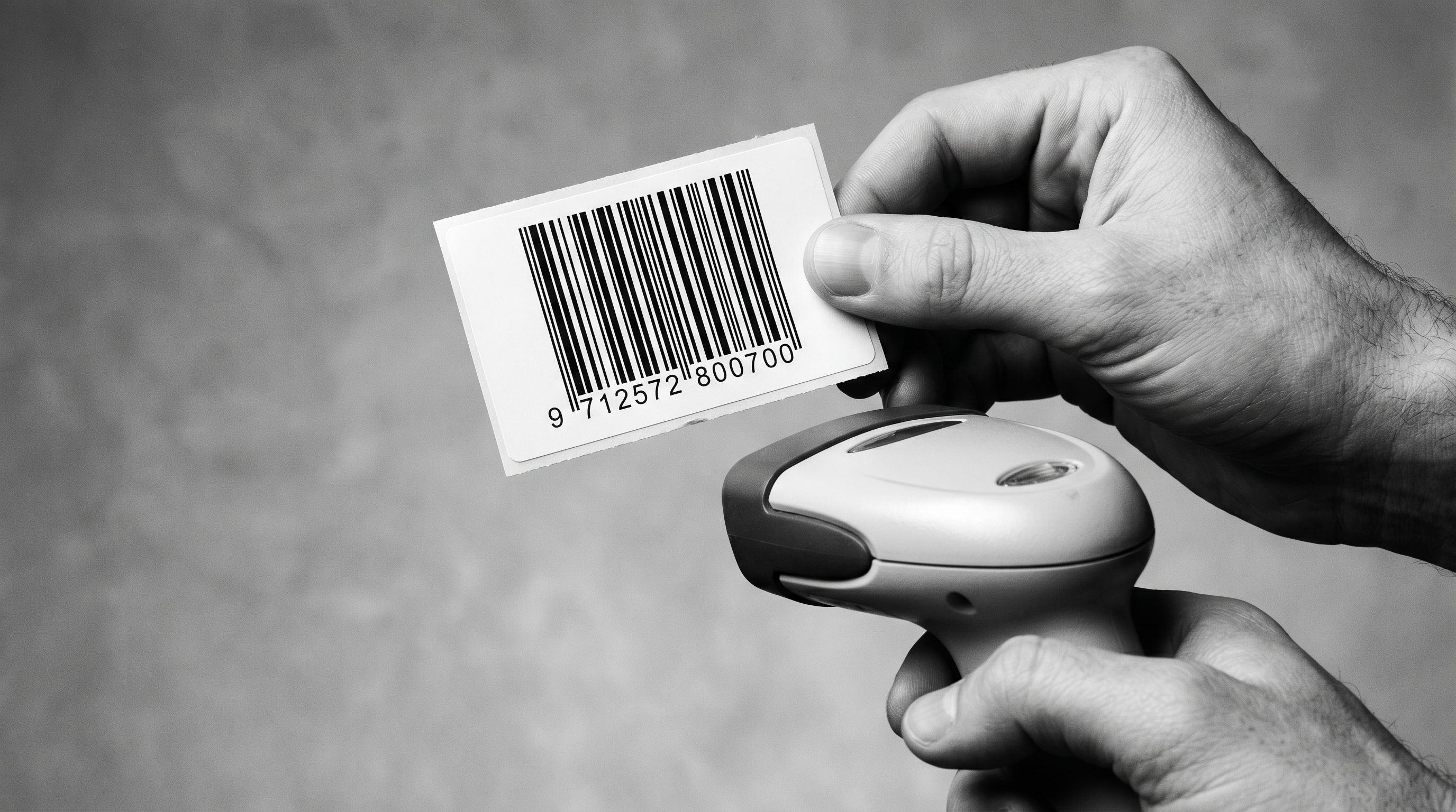 A product barcode label on white stock with a hand-held barcode scanner positioned beneath it at an angle.