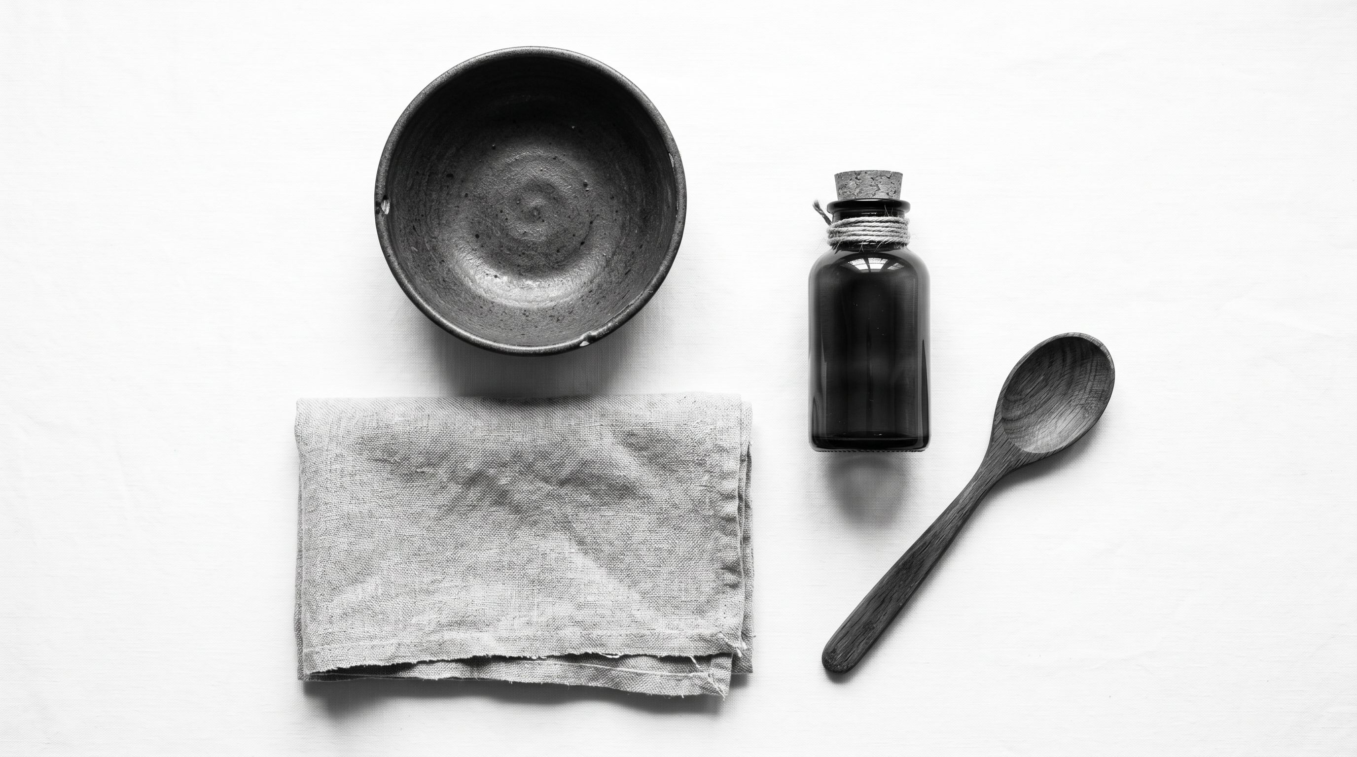 A flat-lay of handcrafted artisan products: a ceramic bowl, folded linen, a small glass bottle, and a wooden spoon.