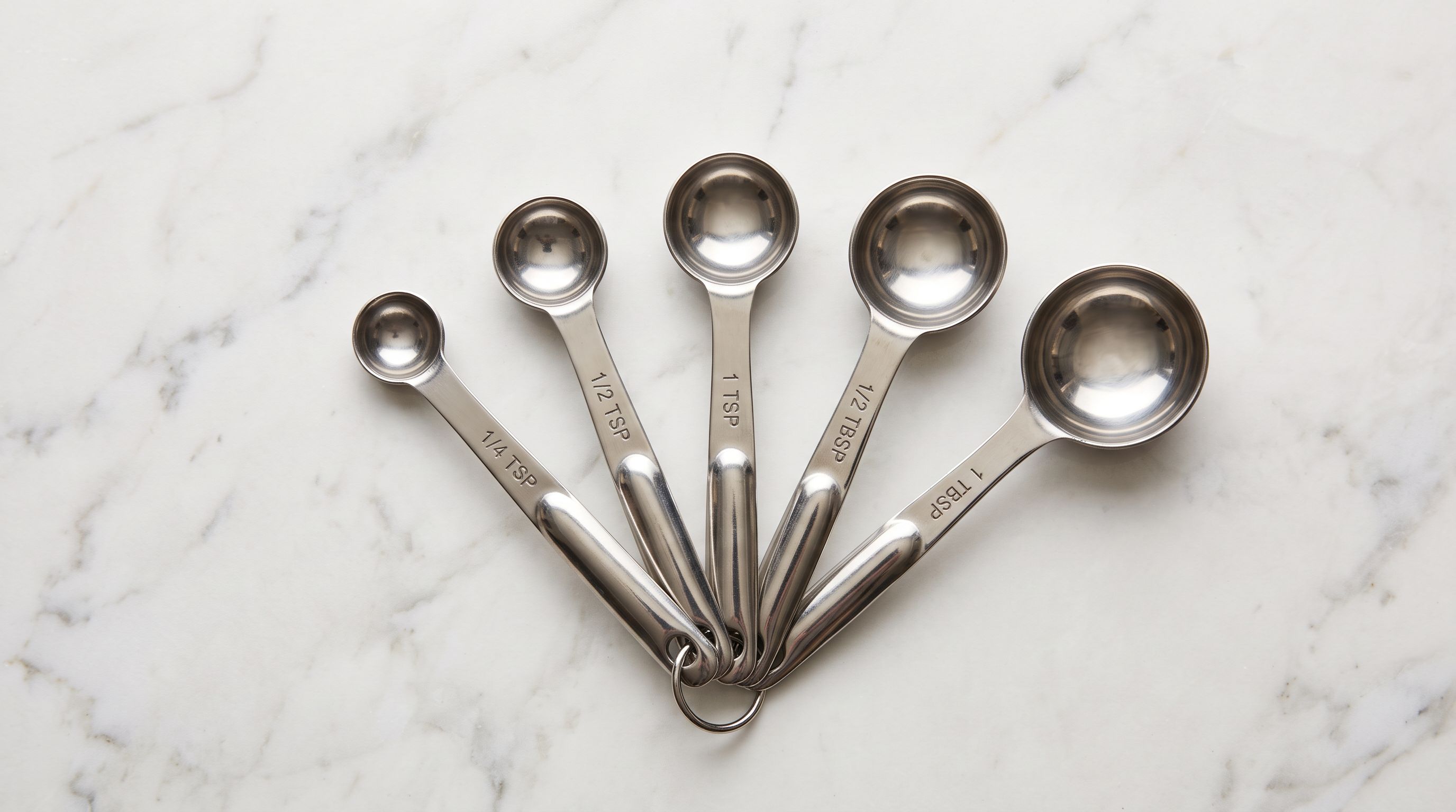 Measuring spoons of graduated sizes arranged in a fan on a marble surface.