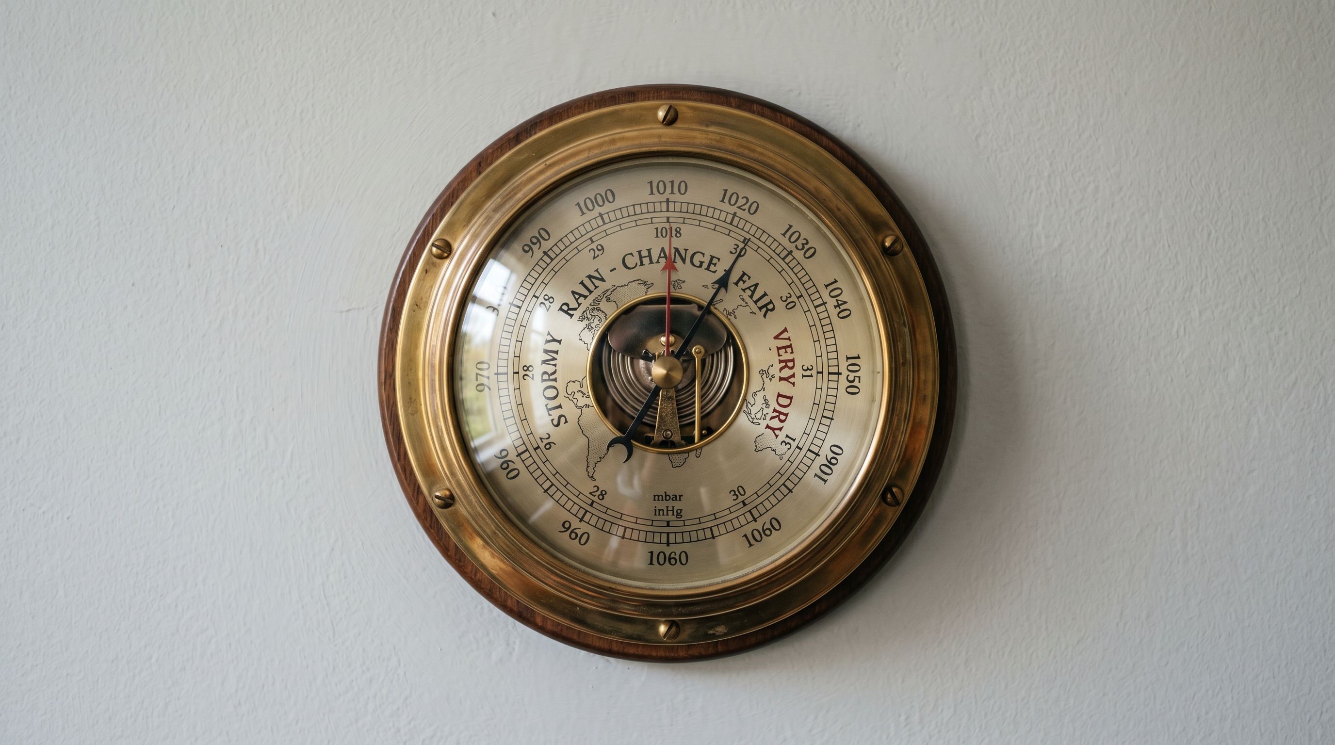 A vintage brass barometer on a pale grey wall, the needle and dial in sharp focus.