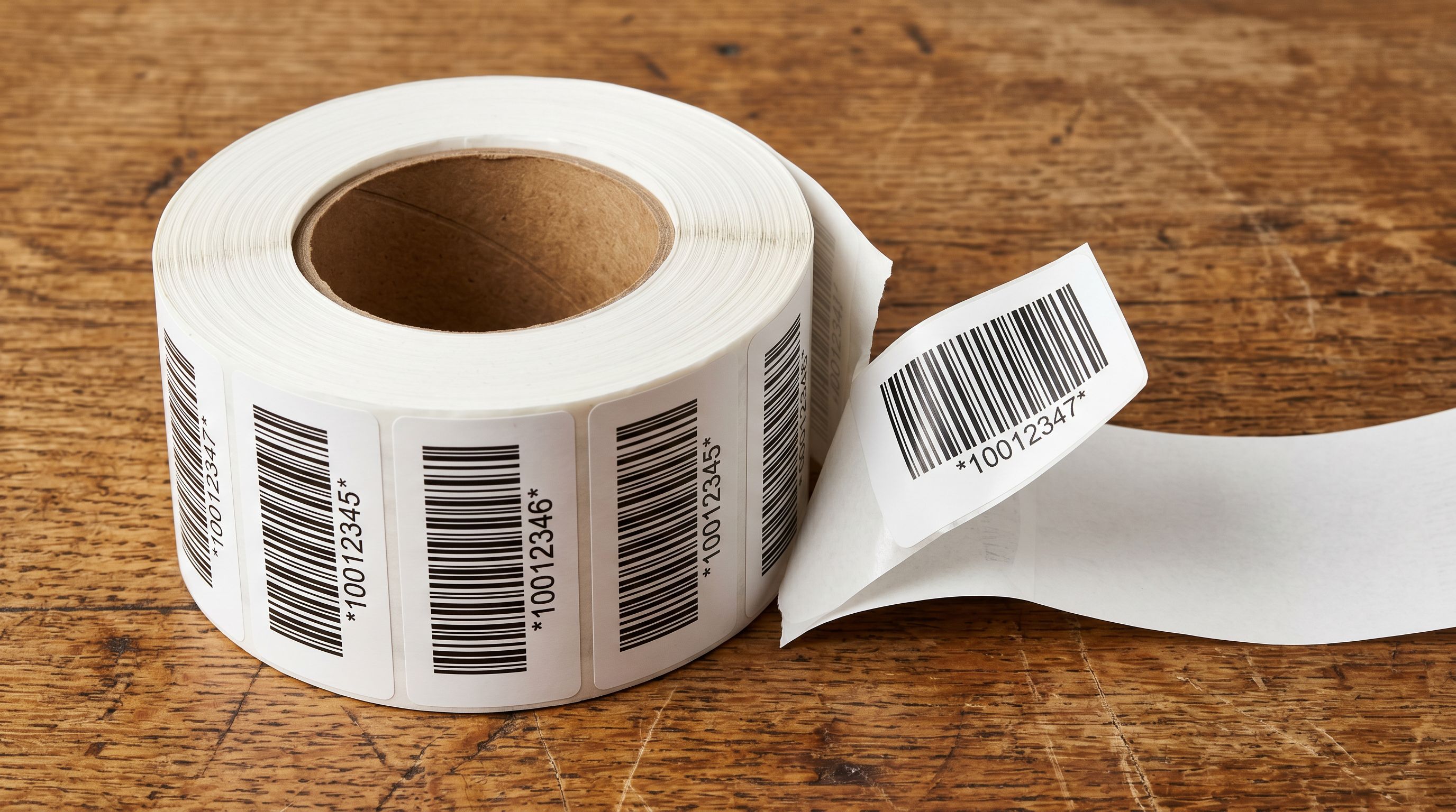 A roll of adhesive barcode label stickers partially unspooled on a wooden surface.