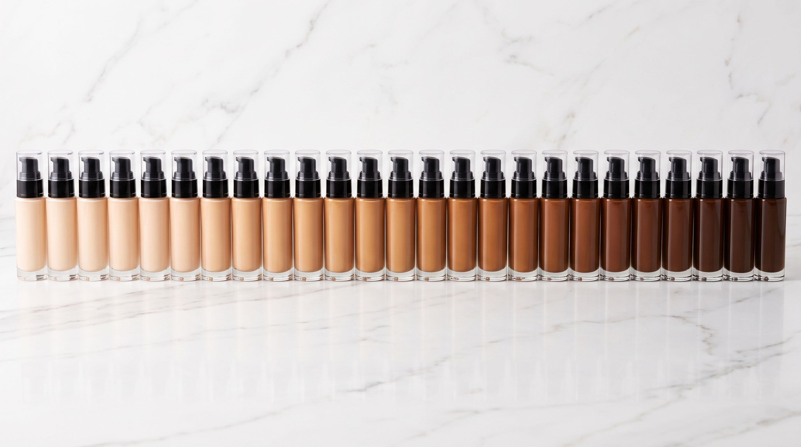 Thirty-eight cosmetic foundation bottles arranged in a precise gradient row from lightest to darkest shade on a white marble surface.