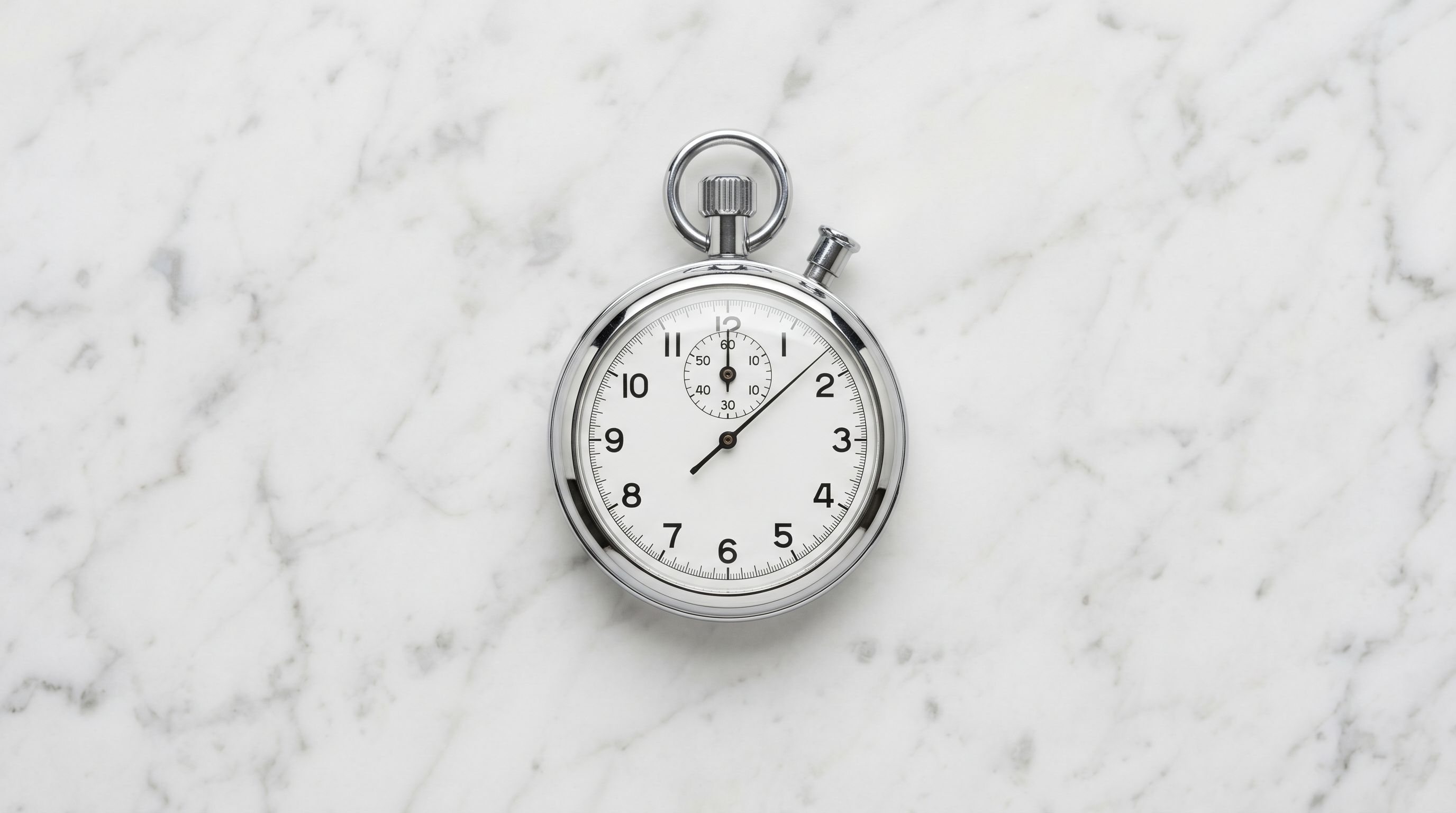 Polished stainless-steel stopwatch placed on smooth white marble surface photographed from above.