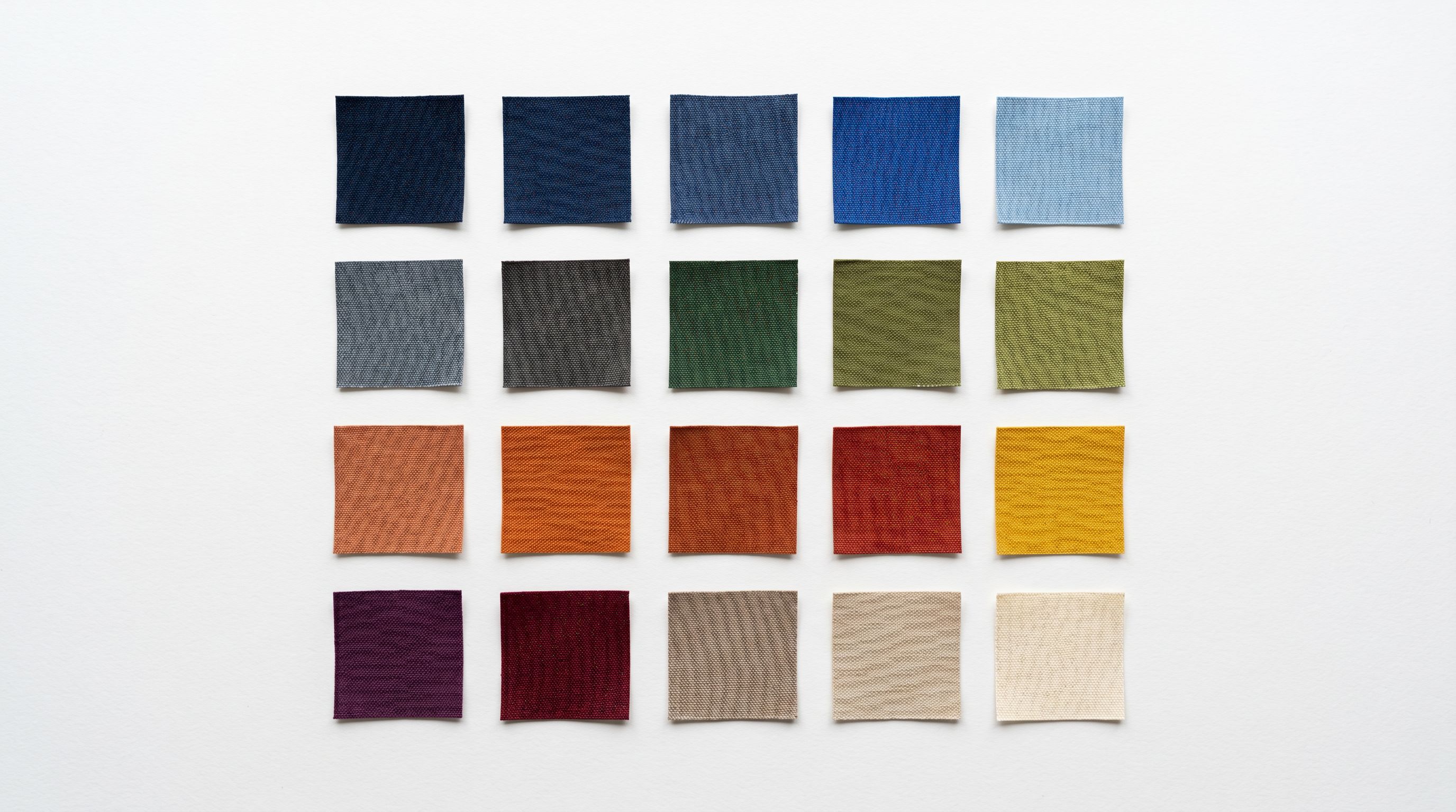 A grid of small fabric colour swatches arranged in neat rows on a clean white surface, each swatch a distinct solid colour, representing product colour variants.