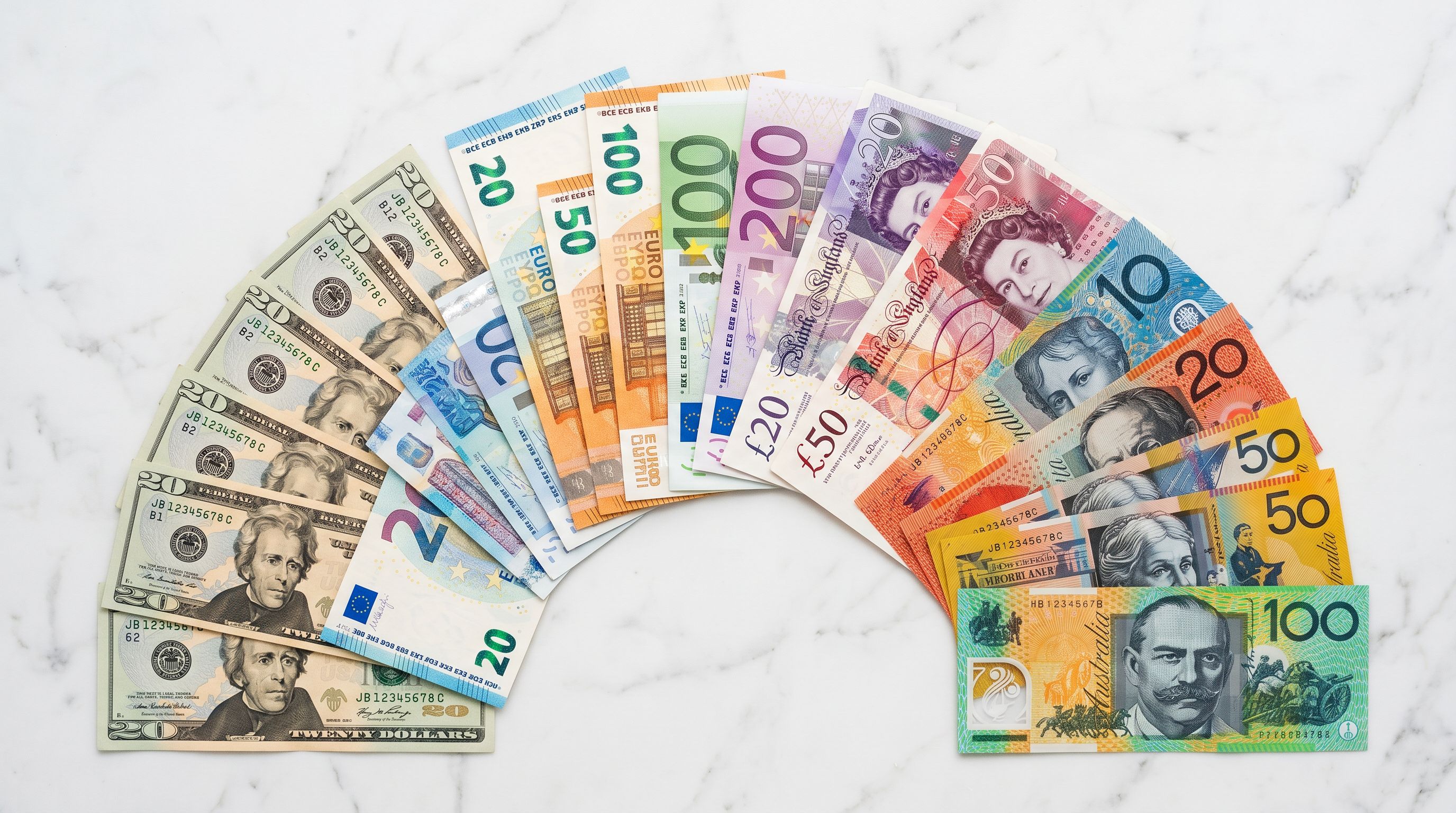 Multiple international banknotes in EUR, USD, GBP and AUD fanned neatly on white marble.