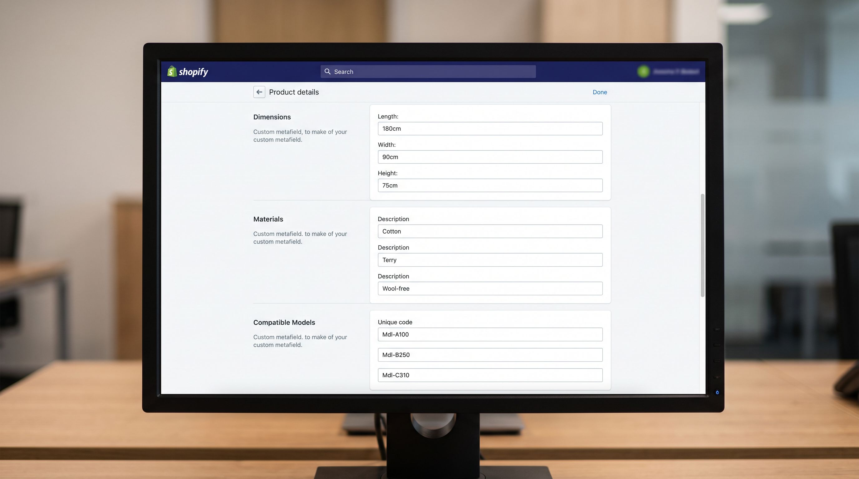 A monitor screen showing a Shopify product admin page with three specification panels: physical dimensions in structured metafields with a green checkmark, material composition in a searchable list metafield, and a compatible models list showing three appliance model numbers, sharp focus, colour photography.