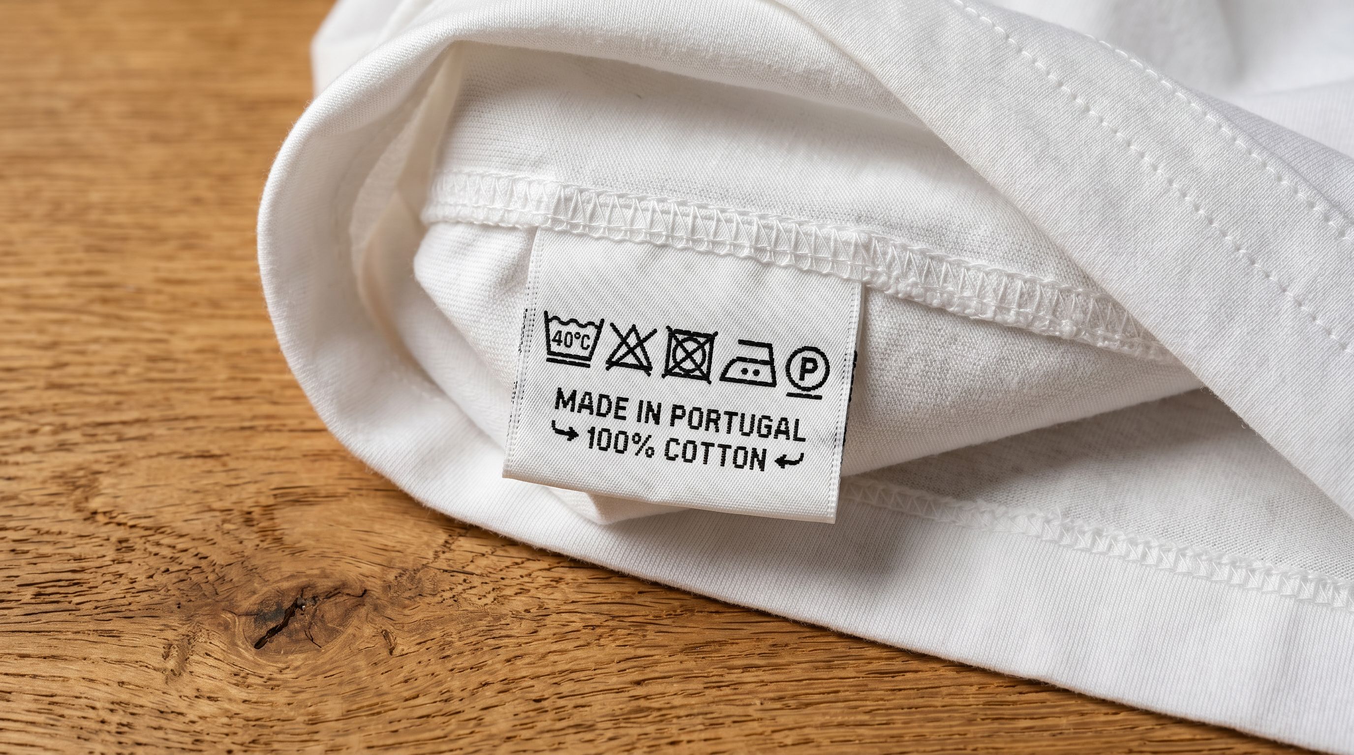 A clothing care label close-up showing wash temperature symbols and fibre content percentages on a garment tag photographed on white fabric.