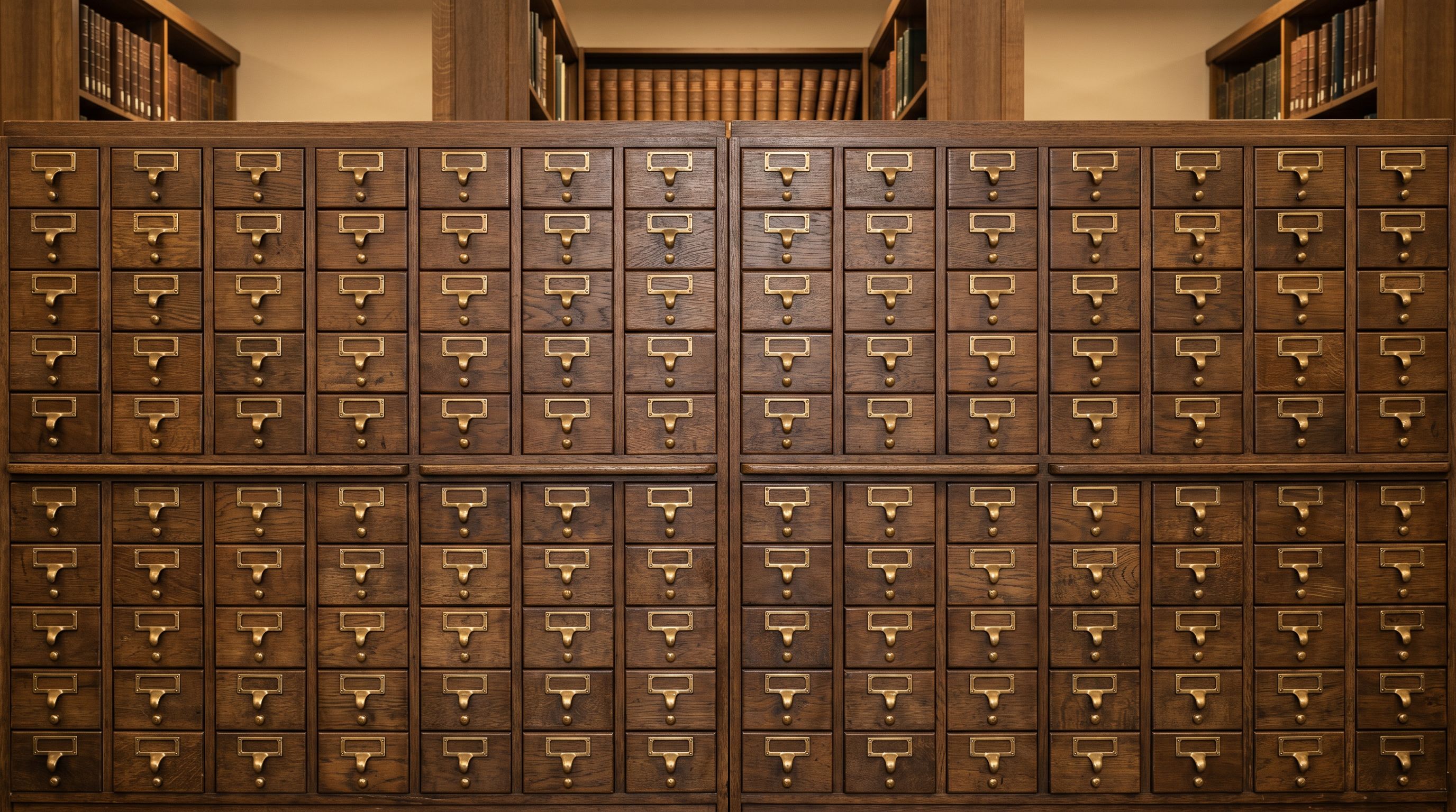 Vintage wooden library card catalogue drawers with brass pull handles arranged in precise rows.